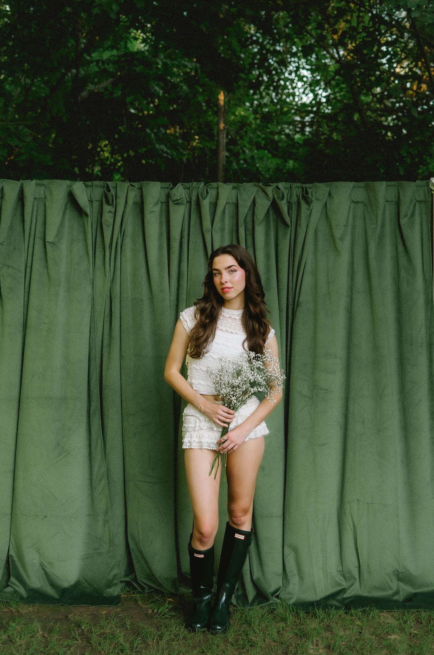 Fashion editorial series against green curtain backdrop with artistic poses.