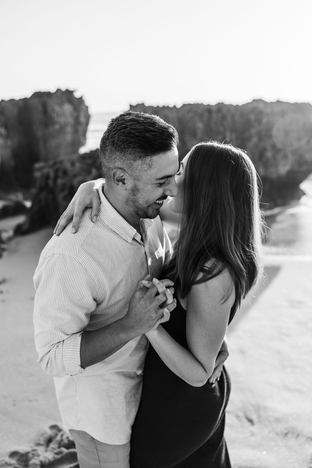 A romantic black and white photo of a couple embracing and dancing together outdoors in natural sunlight.