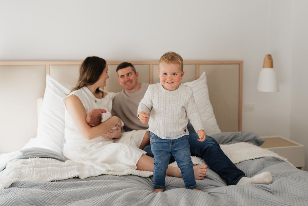 Family shares tender moments together on white bedding in bright, modern bedroom.