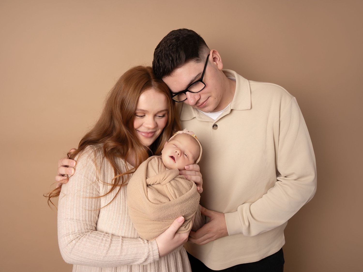 baby girl wrapped swaddled in brown neutral blanket held by mummy and daddy for family photo at newborn photoshoot in Doncaster.