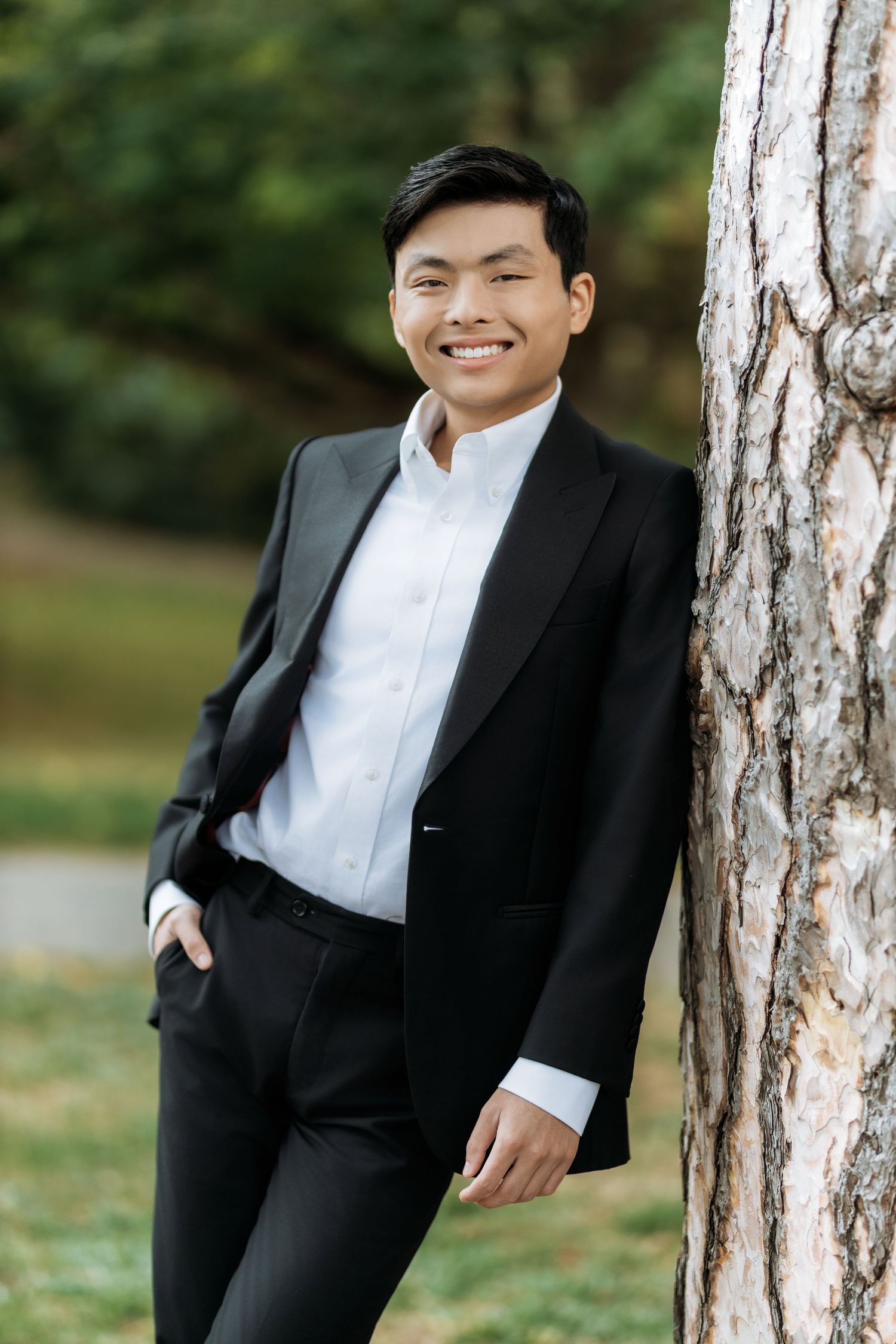 A person in a black suit and white shirt poses playfully against white birch trees in an outdoor setting. Mercer Island Senior Photographer