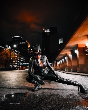 Woman in black Catwoman costume poses dramatically on urban street at night.