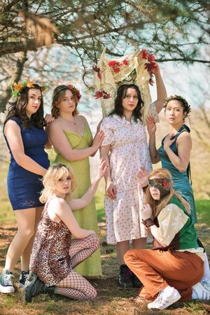 Group of six women in colorful bohemian outfits posing together outdoors under a tree.