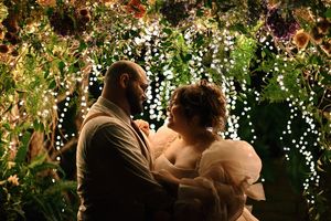 Couple shares romantic moment under floral canopy with fairy lights at wedding reception.
