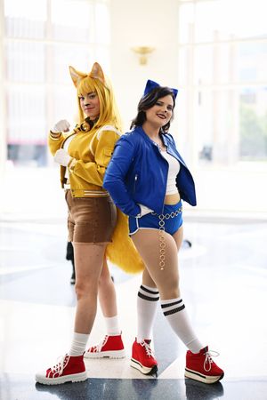 Two women cosplay as fox characters in colorful outfits with animal ears and tails.