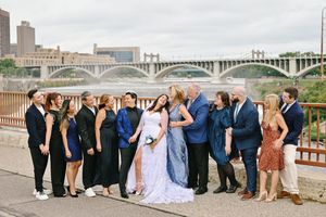 Wedding party group photo on bridge with city skyline and waterfall in the background.