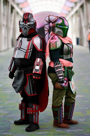 Two cosplayers in detailed Star Wars Mandalorian armor costumes posing back-to-back indoors.