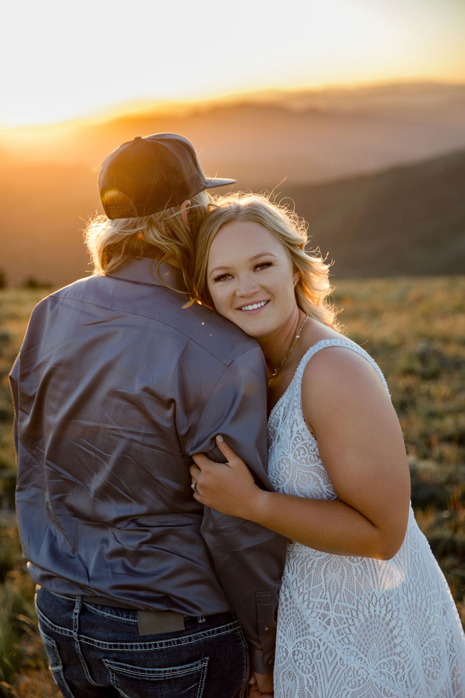 Couple embraces during sunset in field with golden light.
