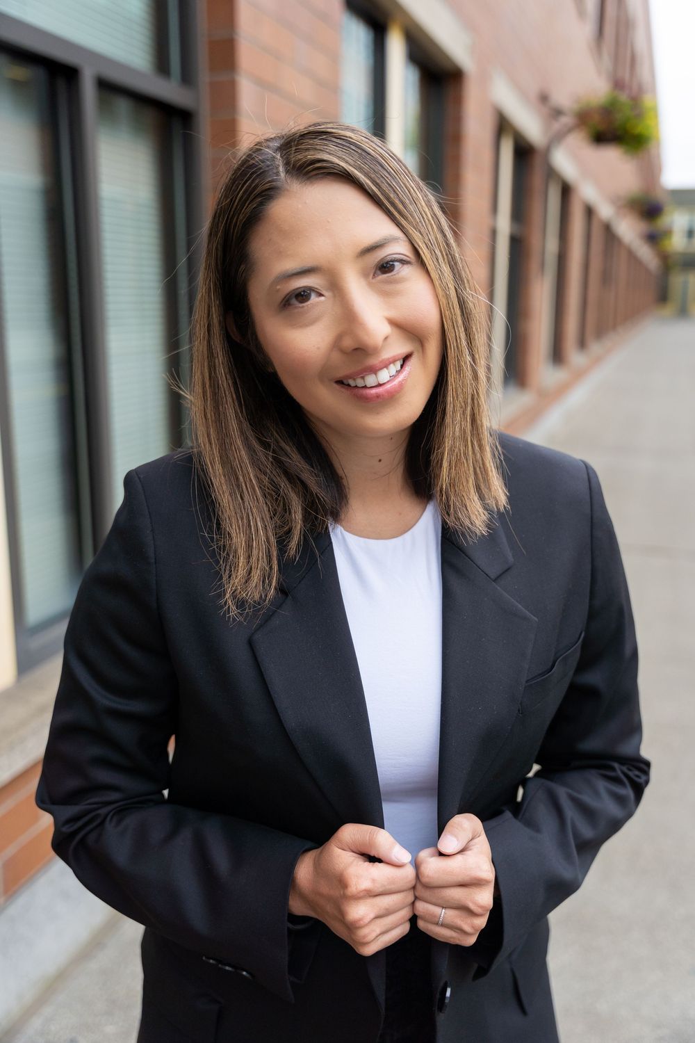 Professional wearing a black blazer and white top stands against brick building exterior.