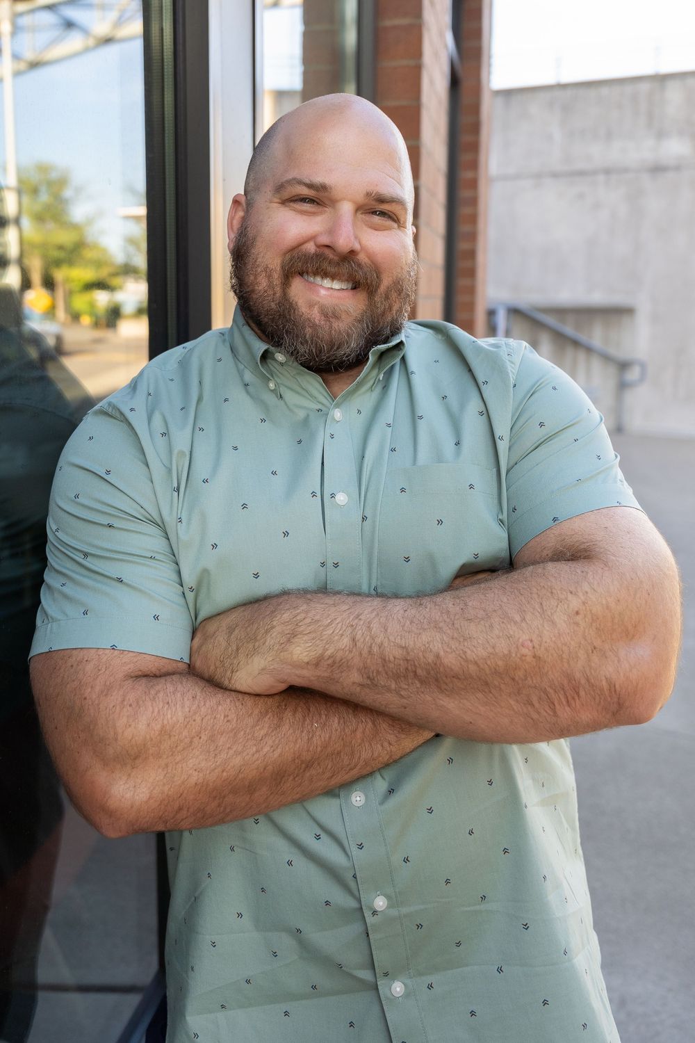 A person wearing a mint green polka dot shirt stands with crossed arms and a cheerful expression.