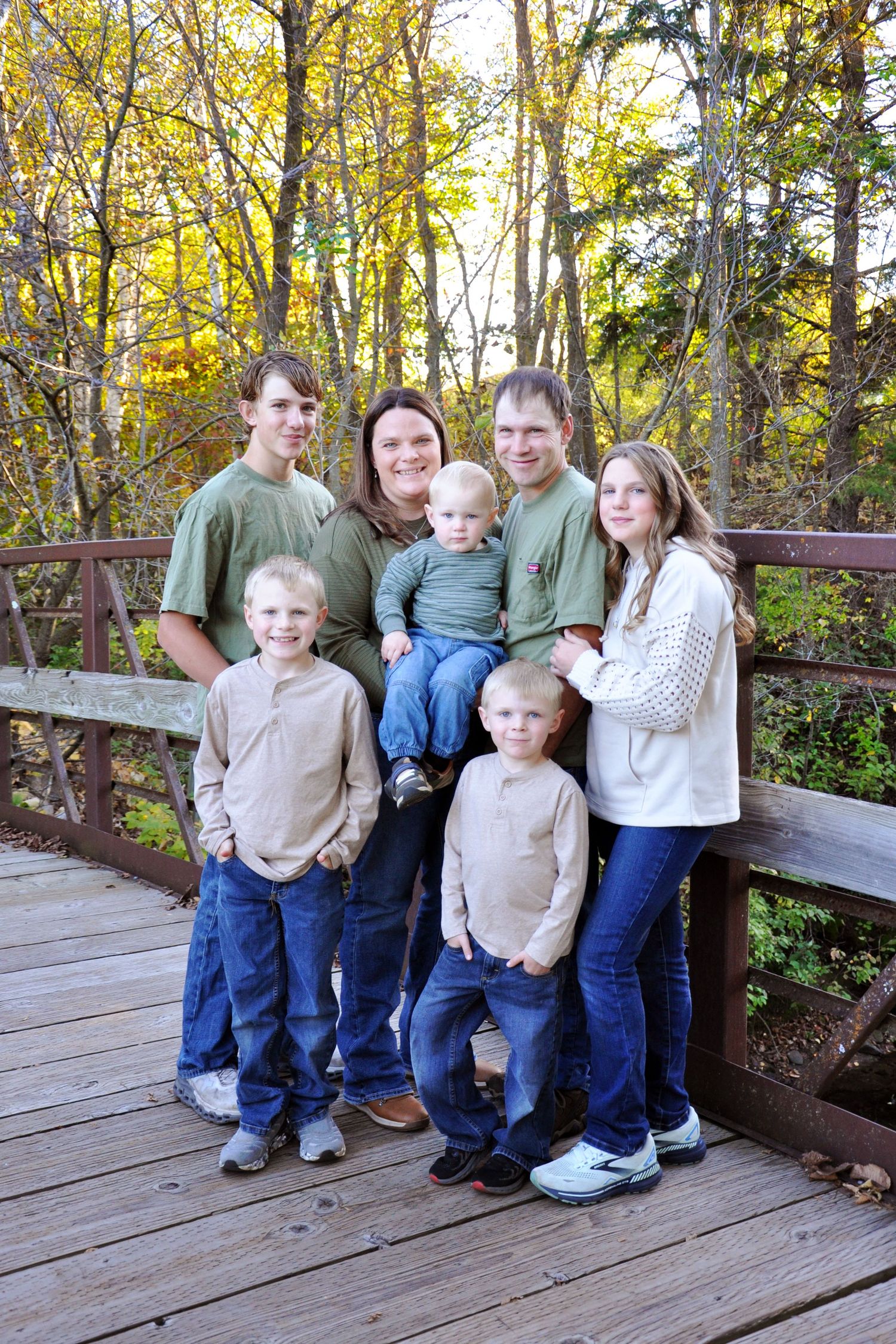 Family group sitting together on wooden deck surrounded by fall foliage.