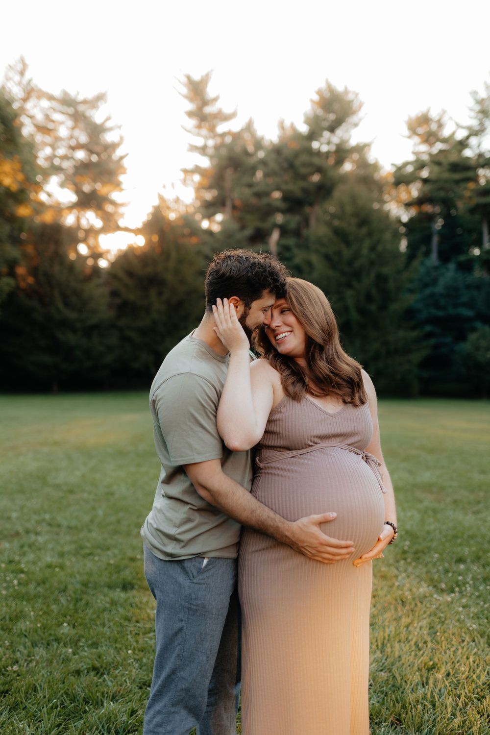Expecting couple shares tender moment in outdoor setting during sunset.