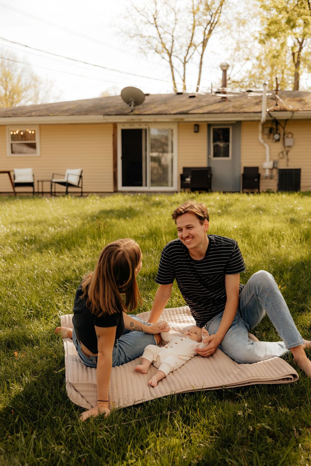 A couple laughs together while sitting on a blanket in their backyard on a sunny day.