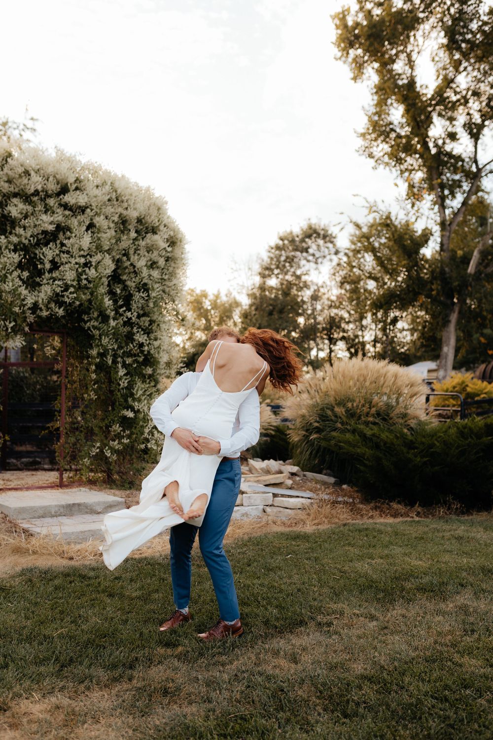 Person in white top and jeans twirling in garden at sunset.