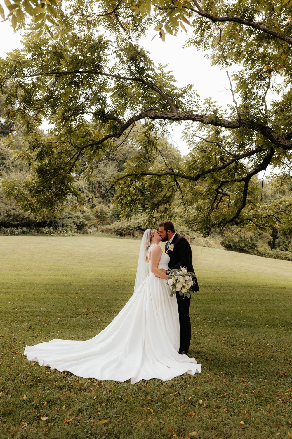 Wedding couple shares intimate moment under trees in garden setting.