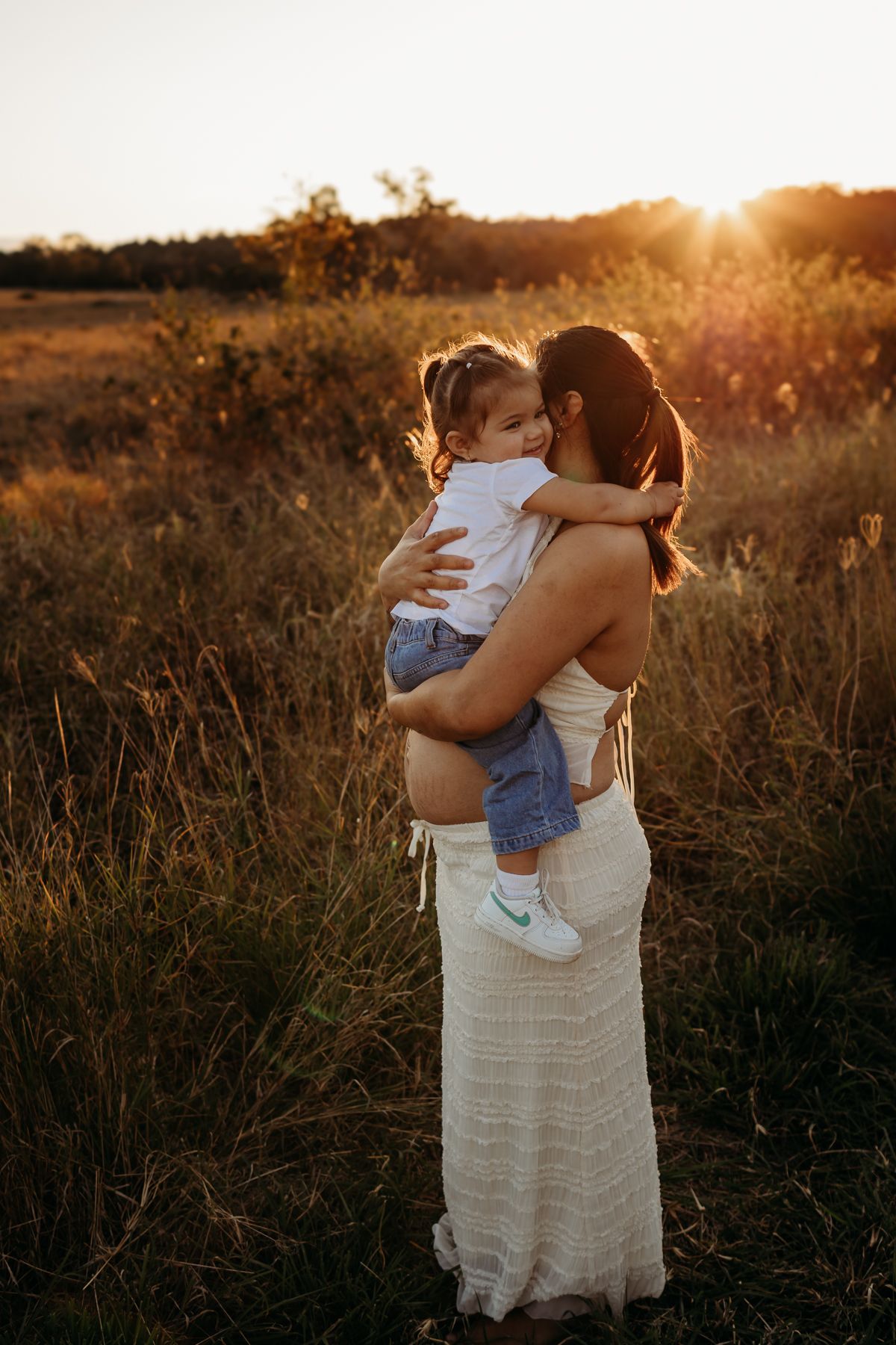 Mother and child embrace in a golden sunset field creating a heartwarming silhouette against the warm evening light.