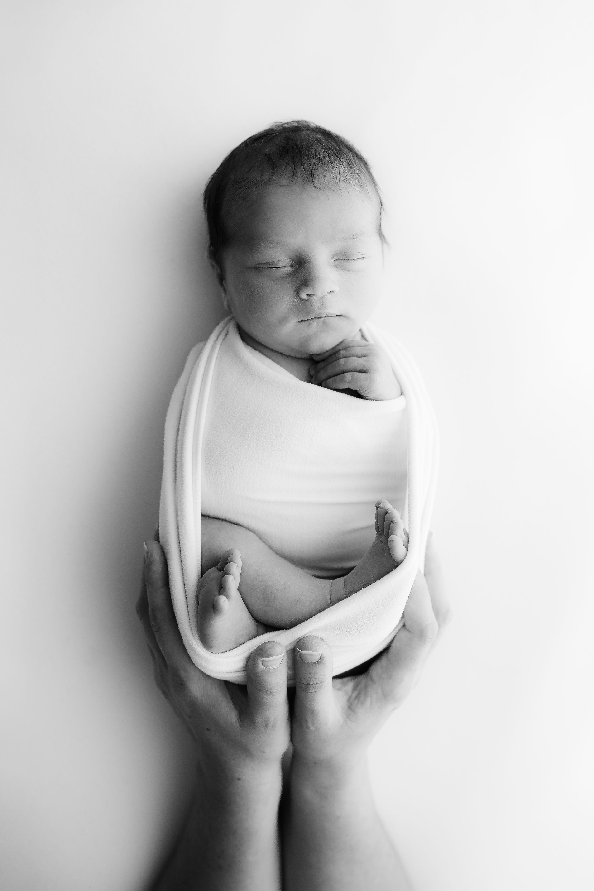 Black and white portrait of newborn baby being gently cradled by hands.
