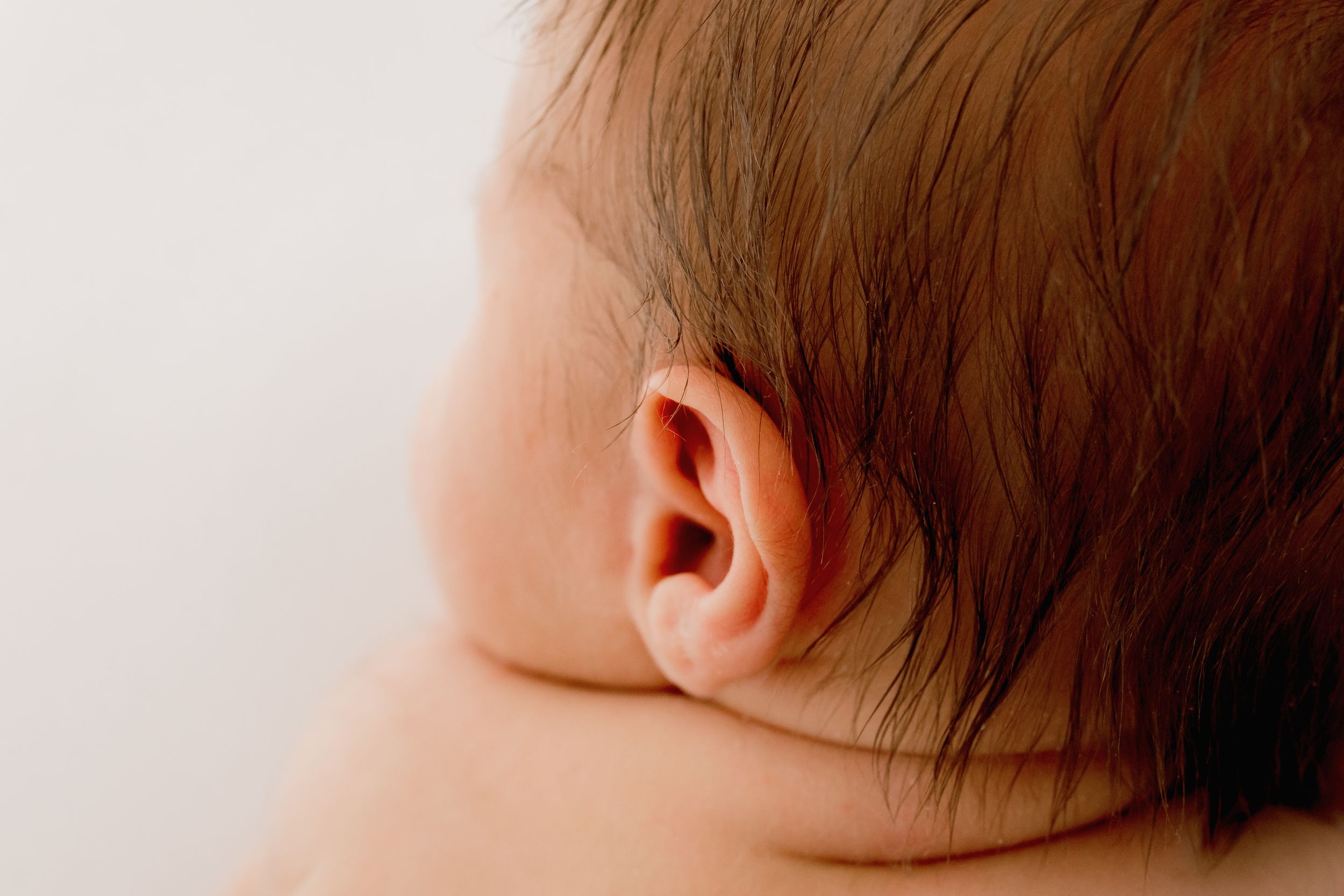 Close-up profile of sleeping newborn baby with soft brown hair.