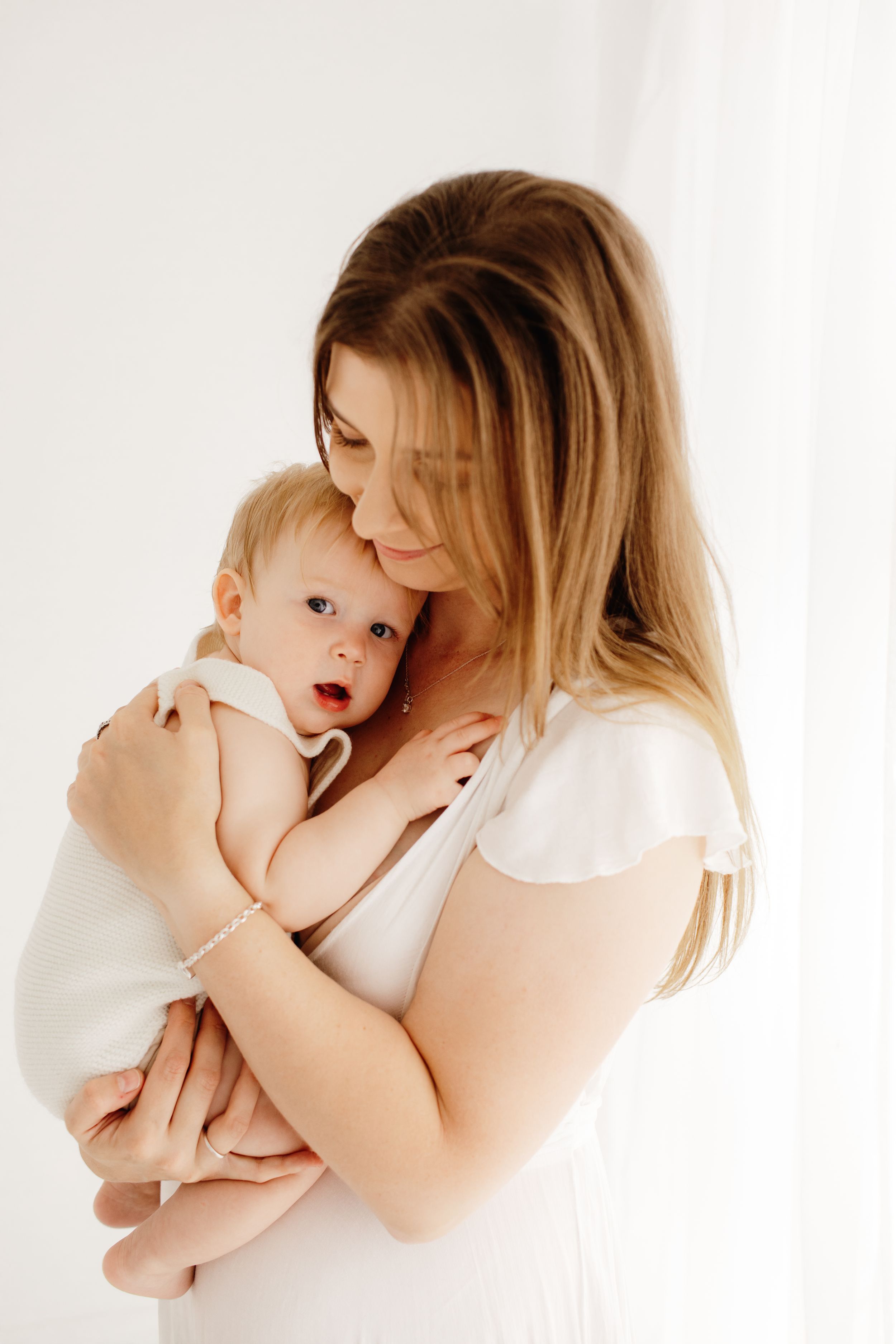 Mother in white embraces baby in series of intimate studio portraits.