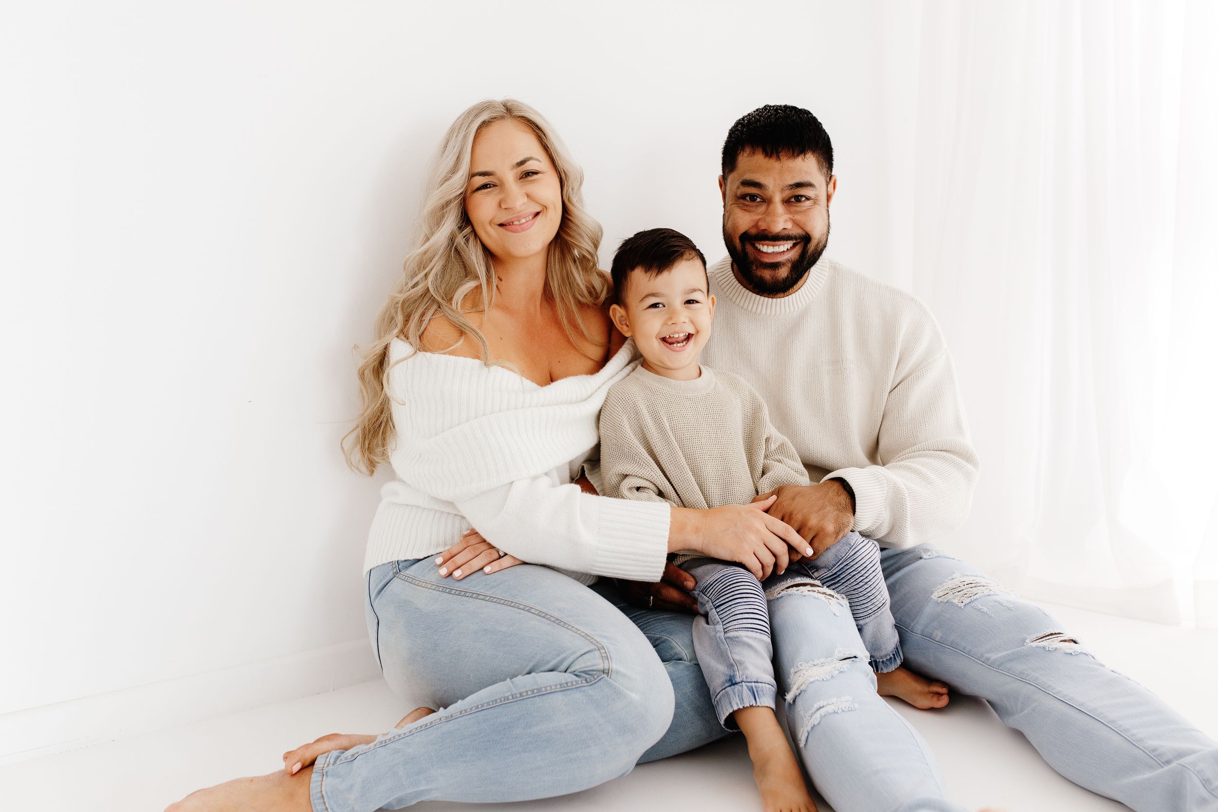 Happy family lounging together on white bed in casual clothing.