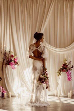 Ethereal wedding dress silhouette against flowing white curtains with floral accents.
