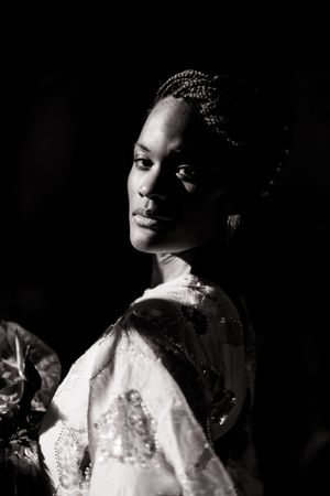 Dramatic black and white portrait with soft lighting showcases intricate braided hairstyle and lace details.