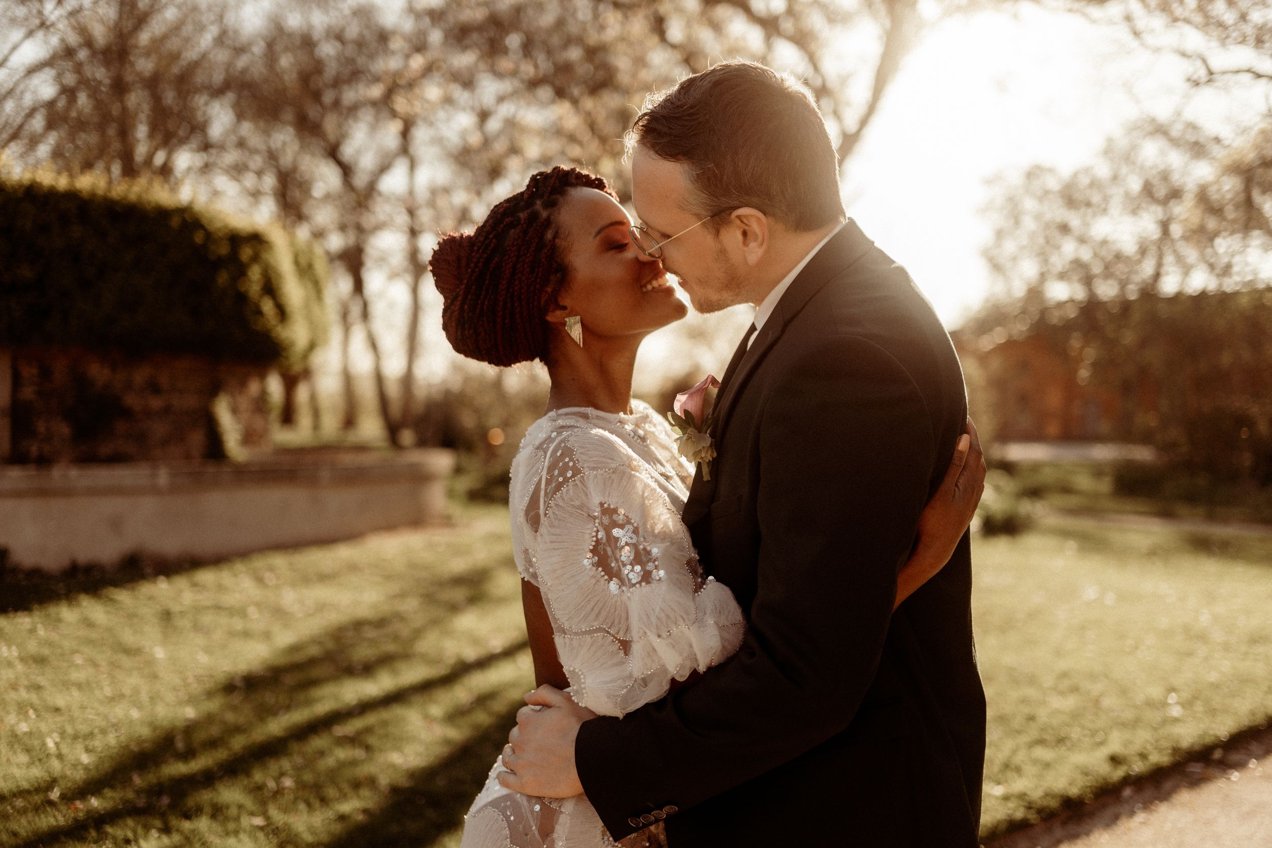 A loving couple shares an intimate moment in a golden sunset-lit park setting wearing elegant wedding attire.