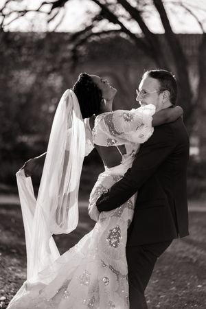 A romantic black and white portrait of newlyweds embracing and dancing outdoors with the bride's veil flowing.