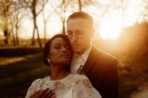 Romantic wedding portrait of couple embracing in golden sunset light against natural outdoor backdrop.