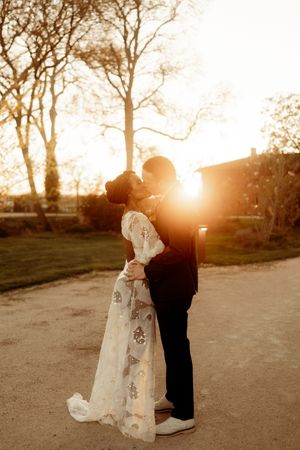 A couple embraces in silhouette against a warm sunset backdrop on a dirt path.