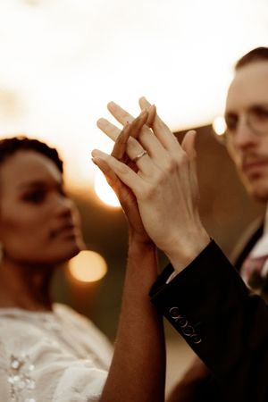 Backs of multiple wedding guests, arms raised in celebration at golden hour with hands visible silhouetted against bright sunlight.