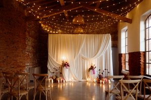 An elegant wedding venue interior decorated with fairy lights and white drapes on exposed brick walls.