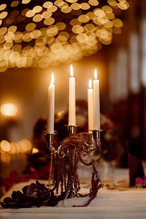 Lit white candles in elegant candelabras cast a warm glow against a dark background with bokeh lights.