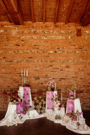 Wedding decor with pink draping and candles arranged against exposed brick walls and wooden beams.