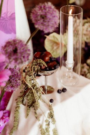 Wedding table decor featuring pink allium flowers, berries in a glass bowl, and a tall candlestick.