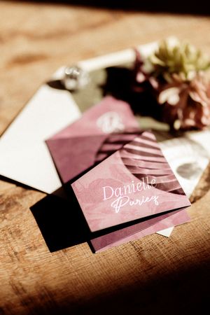 Wedding stationery in dusty rose pink with calligraphy text and floral accents on a wooden surface.