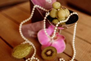 Pearl necklace and pink decorative elements arranged artistically on wood.
