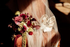 Delicate burgundy and cream bridal bouquet with roses and greenery wrapped in ribbon.