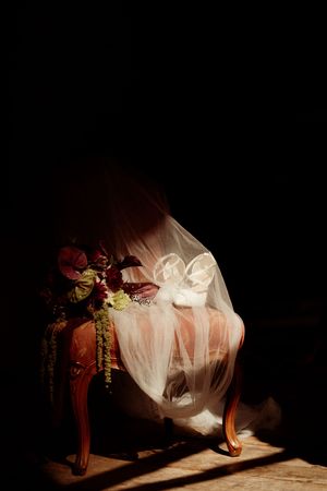 Artistic photo of wedding dress flowing in dramatic lighting with dark background and floral accents.