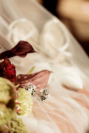 Close-up of wedding dress details with red flower accents and pearl decorations.