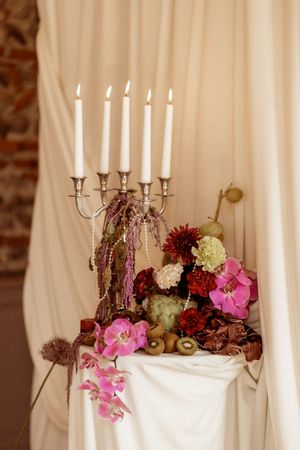 White candelabras adorned with pink and burgundy flowers against a cream fabric backdrop.