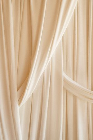 Cream colored fabric curtains with vertical pleats creating soft, elegant draping pattern in natural light.
