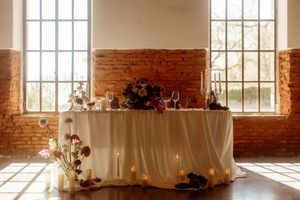 Sunlit wedding reception venue with large windows, exposed brick walls, and white table settings.