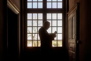 A silhouette of someone reading by a large window with natural backlighting.