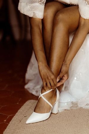 Wedding shoes in white being put on bride's feet in sequence on beige carpet.