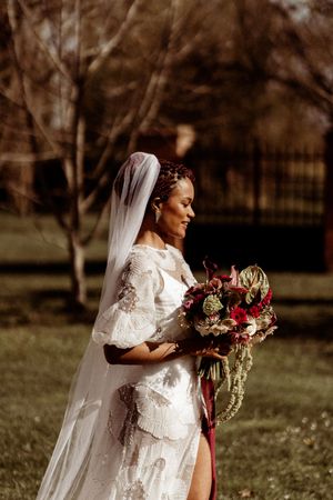 A bride in a vintage-style wedding dress holds a cascading bouquet while standing in golden sunlight.