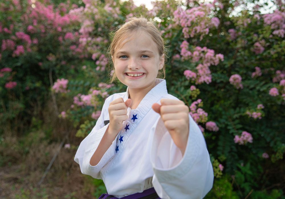 Smiling young girl in white karate uniform with blue stars posing with fists forward outdoors.