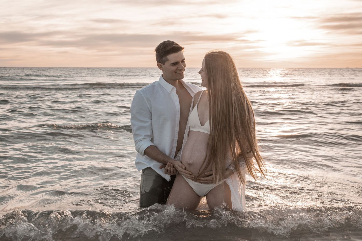Romantic couple holding hands on the beach at sunset in flowing attire.