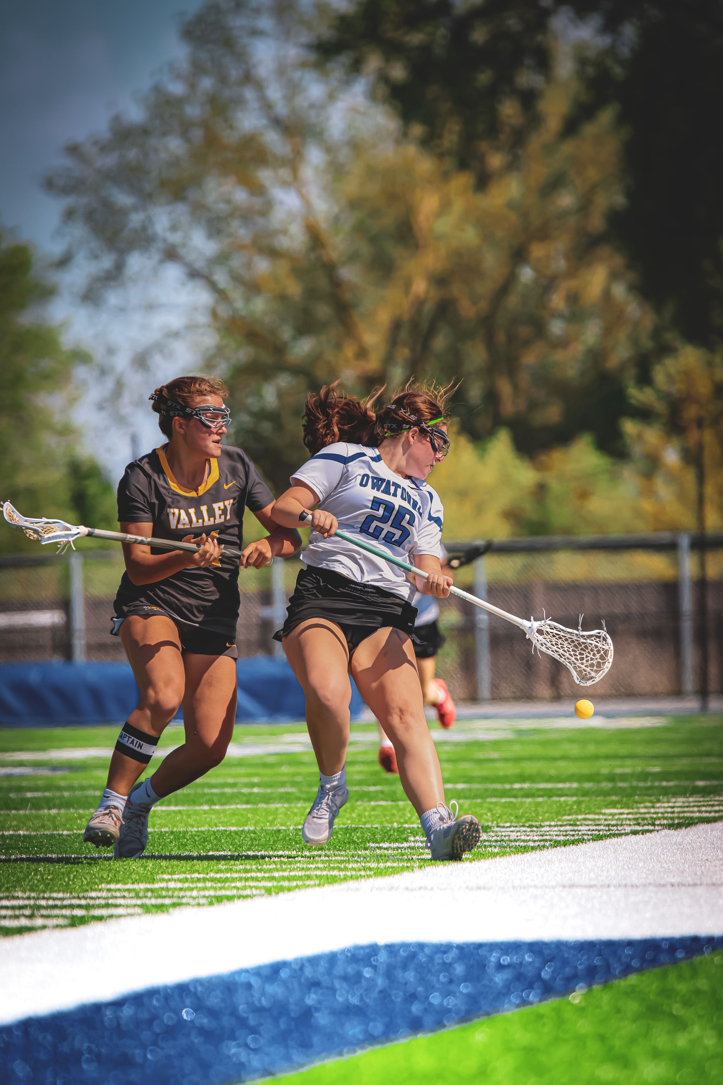 Women's lacrosse players compete intensely during match on turf field.