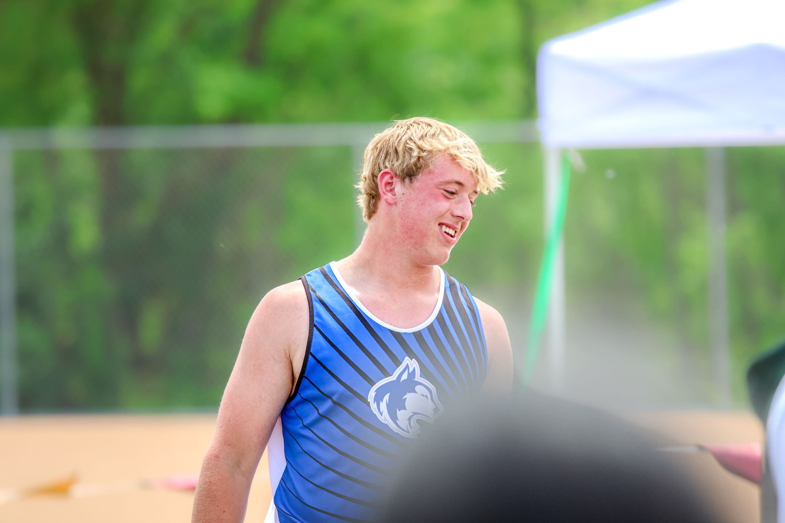 Track athlete in blue tank top smiles during outdoor competition.
